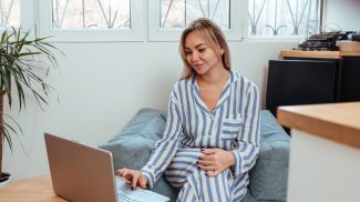 a beautiful woman in pajamas is working on a laptop. the concept of remote work at home and blogging