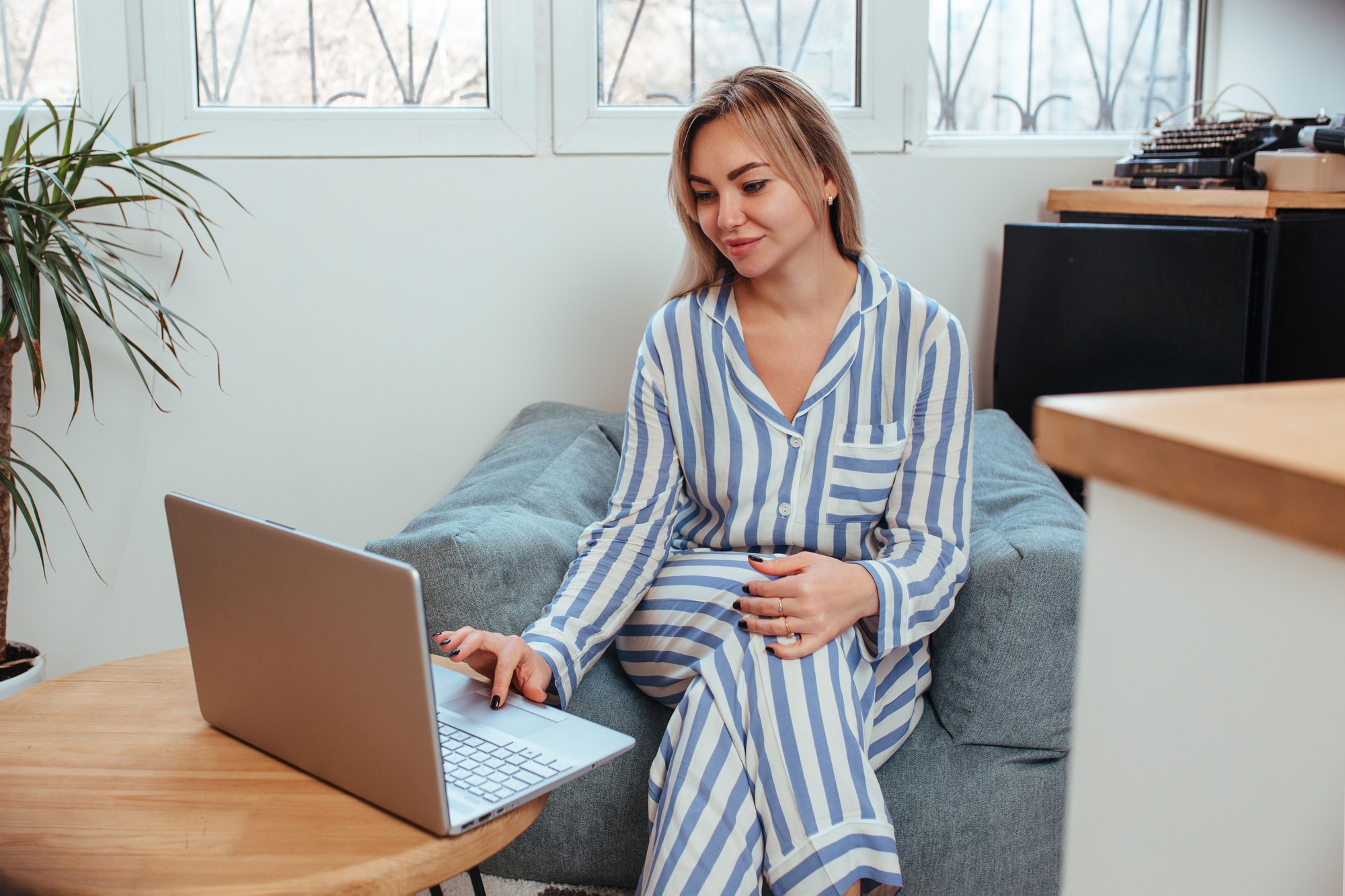 a beautiful woman in pajamas is working on a laptop. the concept of remote work at home and blogging