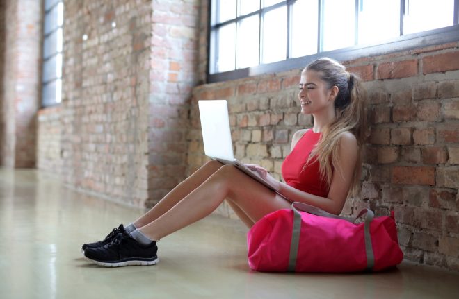 Attractive young female working on the laptop sitting next to her gym bag