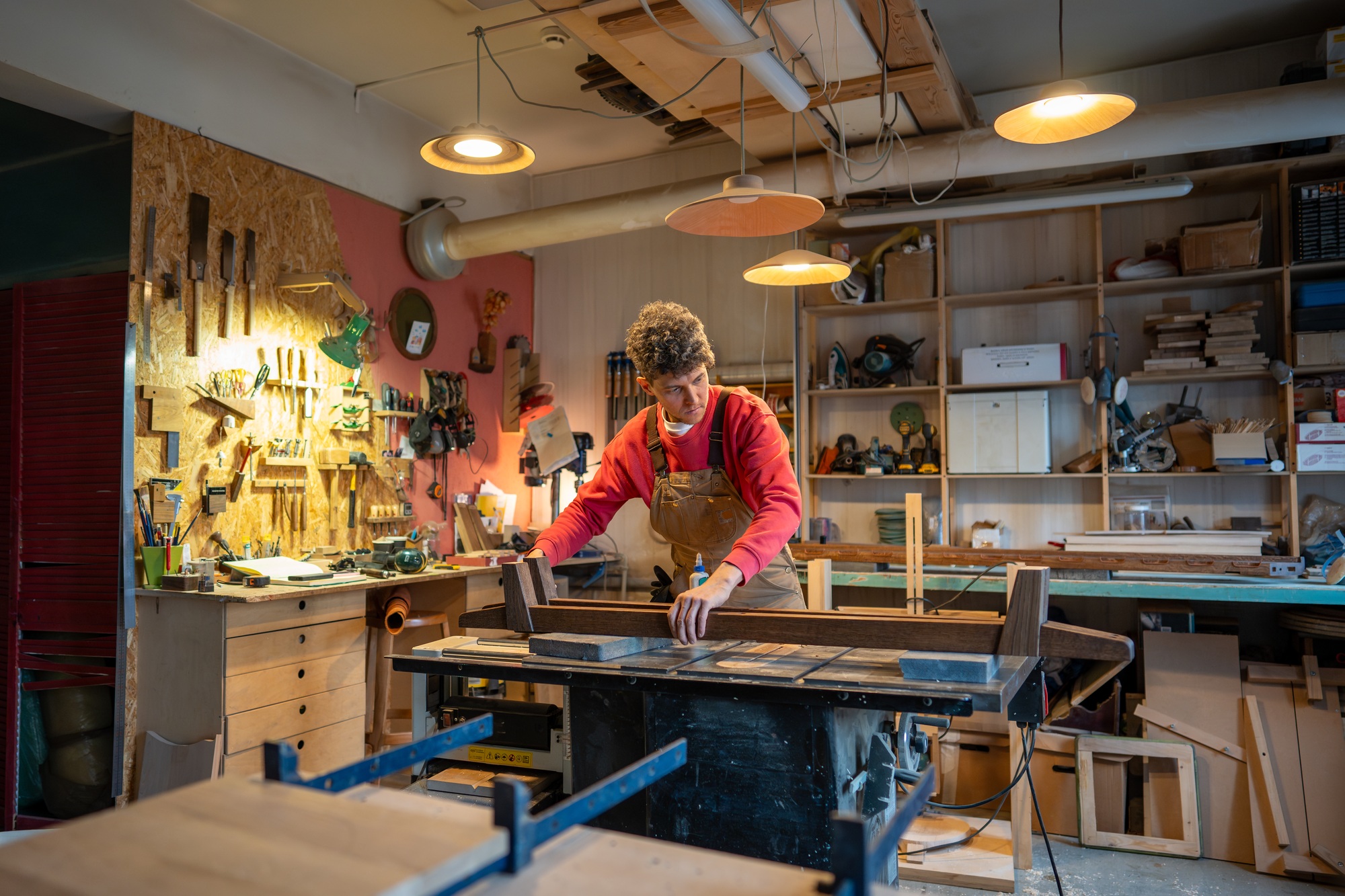 Concentrated man carefully working in carpentry creative studio, engaged in creation of bed.