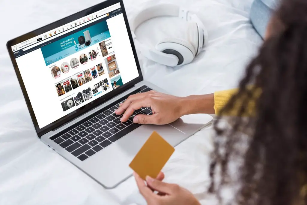 cropped image of woman holding credit card and using laptop with amazon  on screen