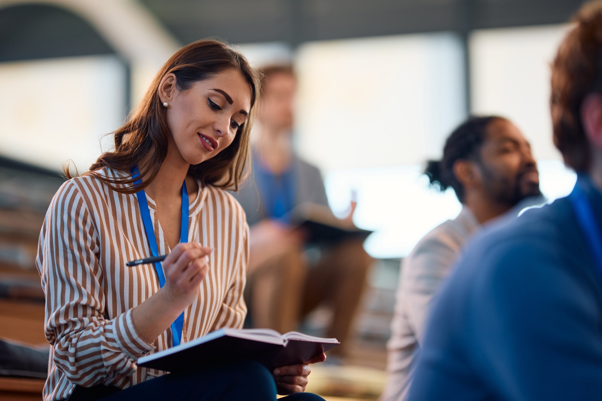 Female entrepreneur taking notes while attending a business seminar in conference hall.
