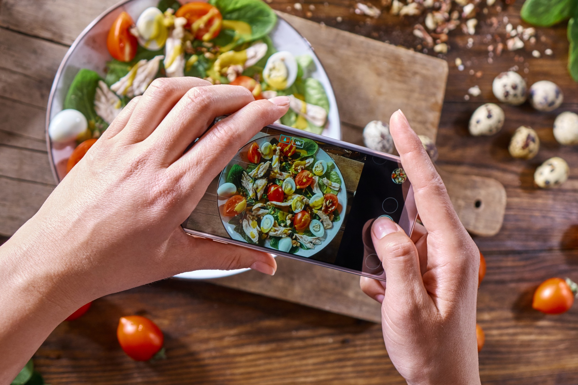 Hands of a girl with a phone make a photo of a freshly prepared salad. Food blogging concept. Top