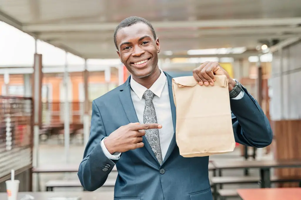 man in suit and tie points to paper bag with copy space for text or logo