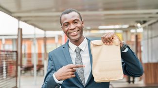 man in suit and tie points to paper bag with copy space for text or logo