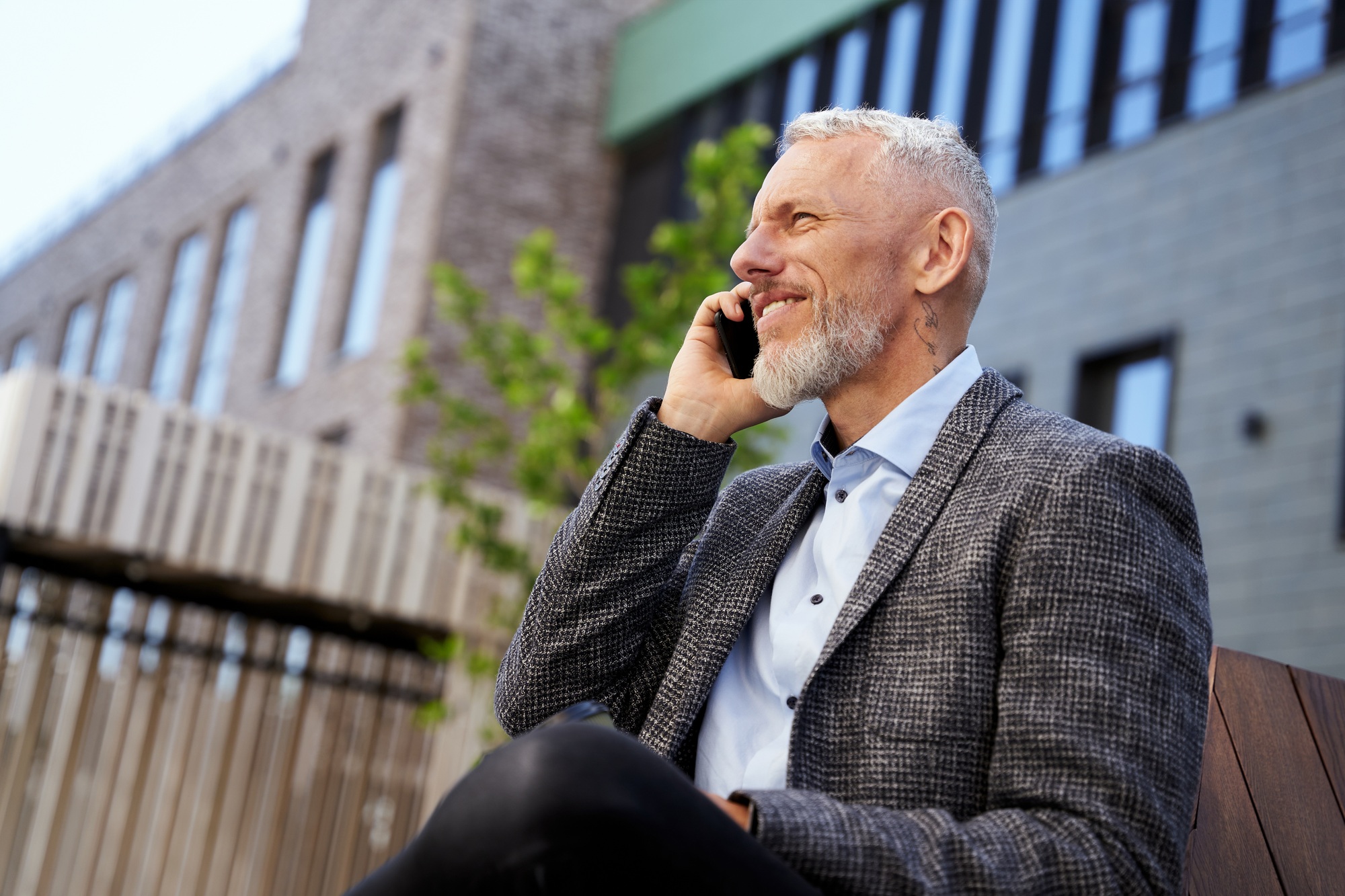 Portrait of elegant mature businessman talking on the phone while taking a break, sitting on