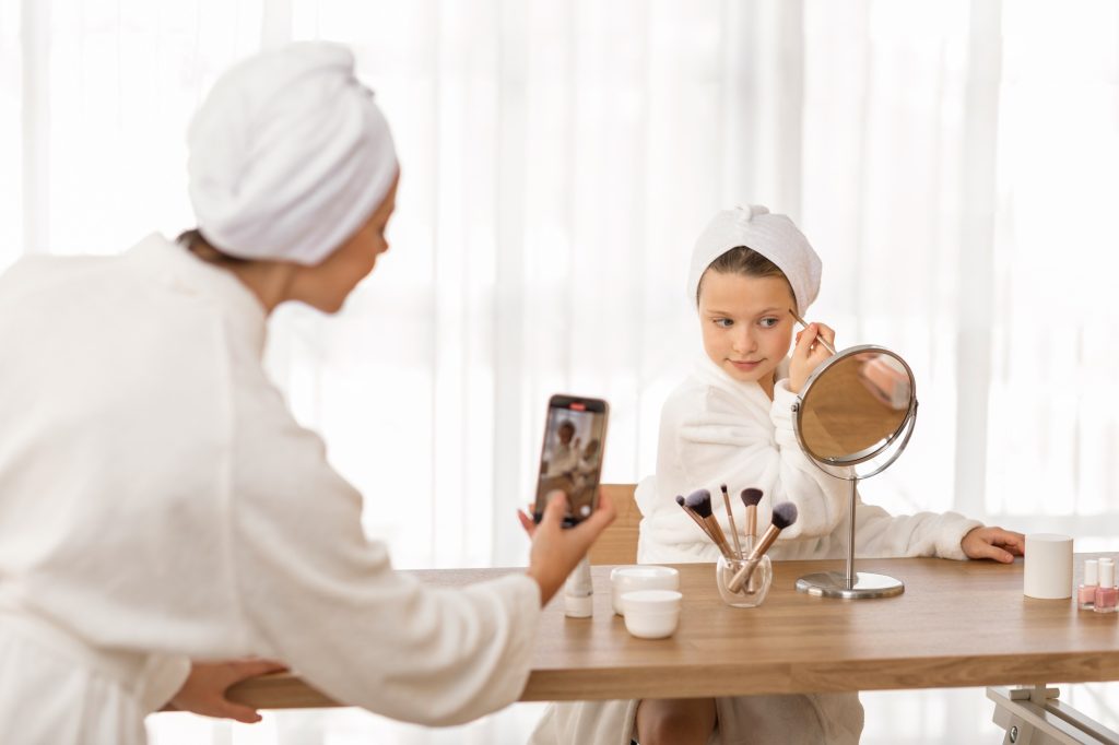 Sharenting Concept. Mom recording video of her little daughter doing first makeup