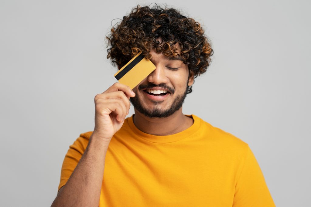 Smiling attractive Indian man holding credit card isolated on gray background. Shopping, sales