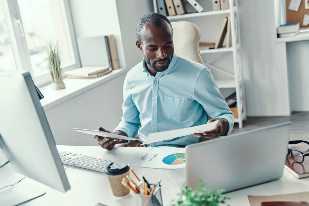Top view of concentrated young African man in shirt analyzing sales data while working in the office