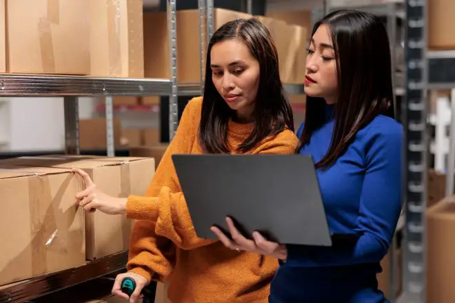Warehouse delivery managers using order processing system on laptop