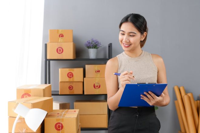 Woman checking inventory with clipboard in hand, surrounded by cardboard boxes